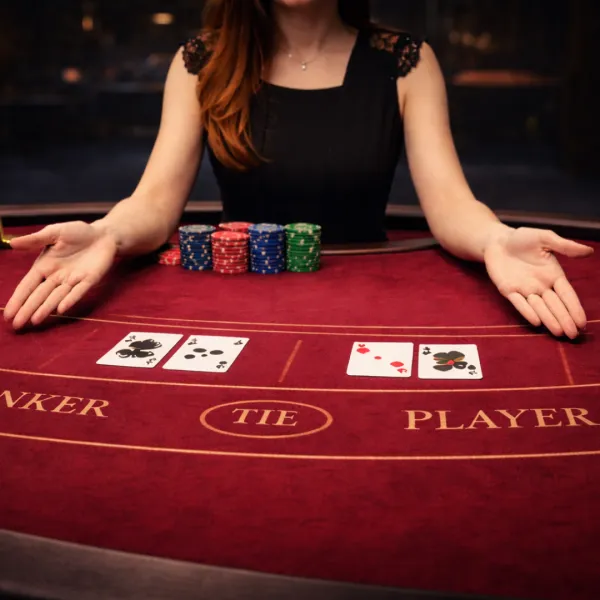 Live dealer presenting dealt cards and stacks of casino chips on a red felt table in the Black Jack live game by Evolution Gaming
